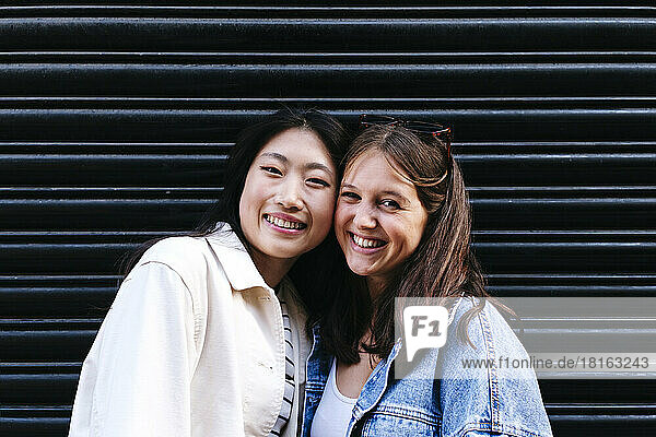 Happy lesbian friends with cheek to cheek in front of shutter