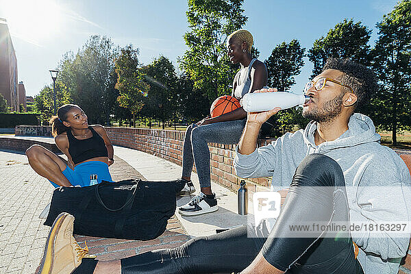 Sportsman drinking water by friends on sunny day