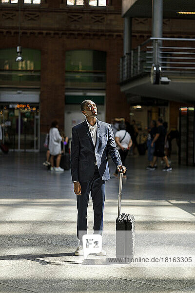 Young businessman with luggage standing at railroad station