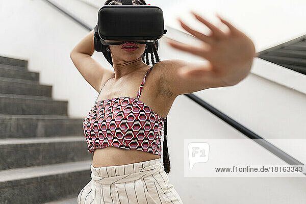 Woman wearing virtual reality simulator gesturing on staircase
