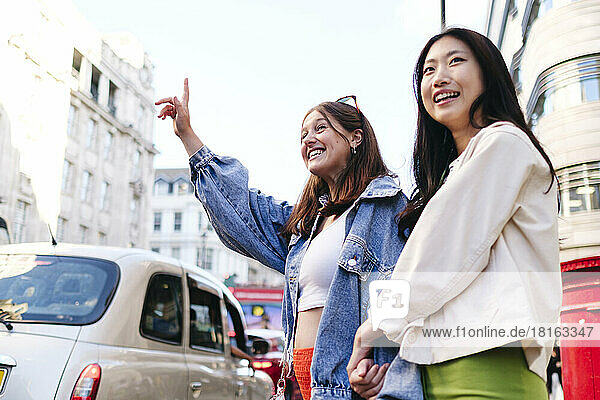 Happy lesbian couple hailing ride standing in city