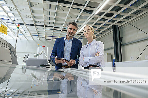 Confident mature businessman with colleague examining 3D printing machine at factory