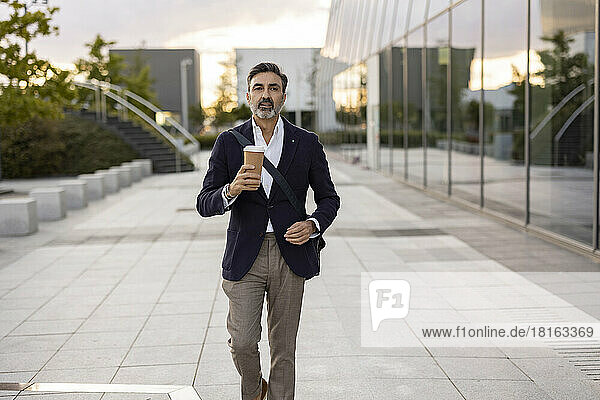 Businessman with disposable cup walking by office building