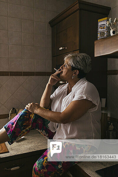 Woman smoking cigarette in kitchen