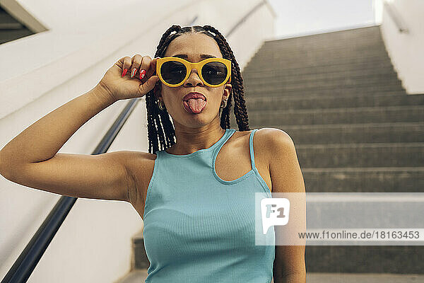 Young woman wearing sunglasses sticking out tongue on staircase