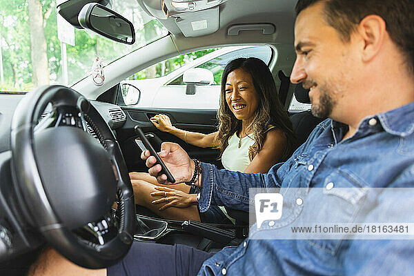 Smiling woman looking at man using smart phone sitting in car