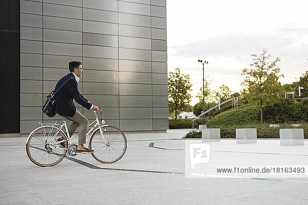 Businessman riding bicycle in front of office building