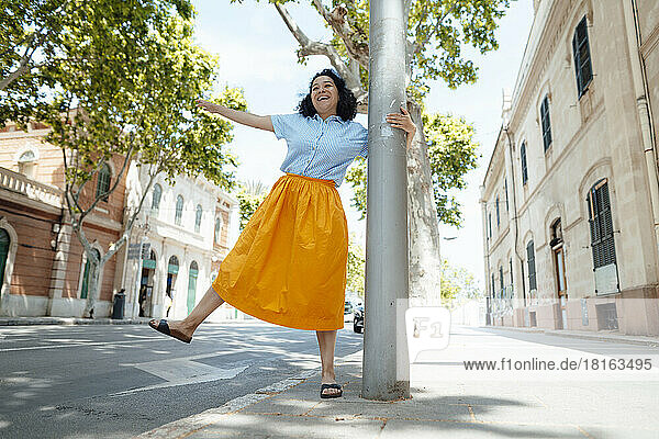 Playful woman holding pole dancing on sidewalk in city