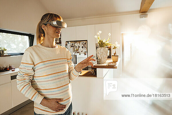 Pregnant woman touching belly wearing virtual reality headset at home