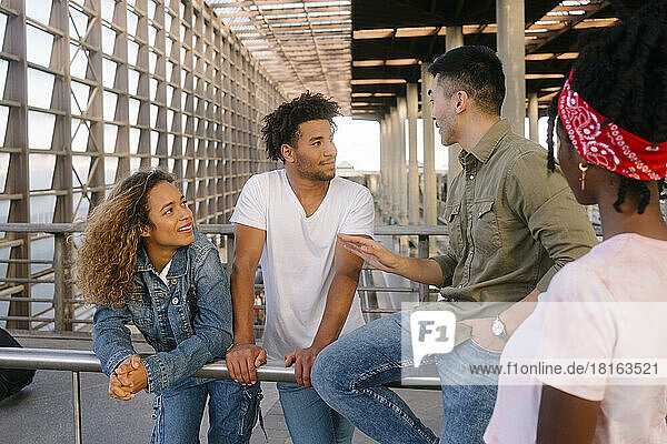 Young man gesturing and talking to multiracial friends at railroad station