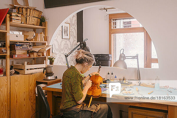 Instrumentenbauer mit Pinsel und Polieren der Geige am Schreibtisch in der Werkstatt