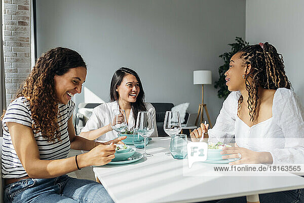 Fröhliche Freunde essen Salat am Esstisch im Wohnzimmer