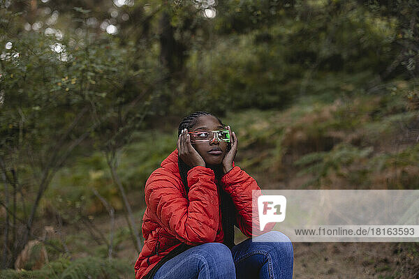 Young woman wearing futuristic glasses sitting in forest