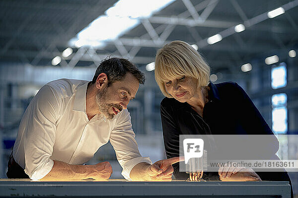 Smiling businesswoman with colleague examining machine part in industry