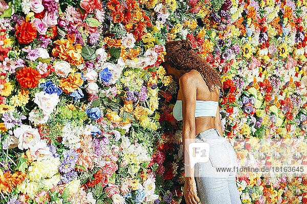 Junge Frau mit lockigem Haar lehnt mit dem Kopf an die Blumenwand