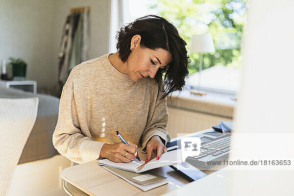 Mature businesswoman writing in note pad on table at home