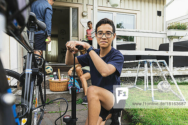 Smiling boy inflating bicycle tire outside house