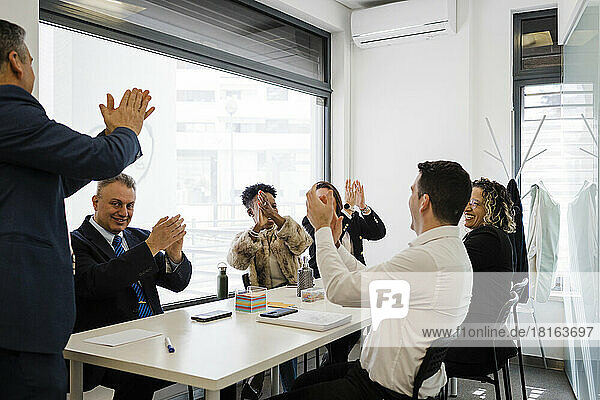 Happy business colleagues applauding together in meeting at office