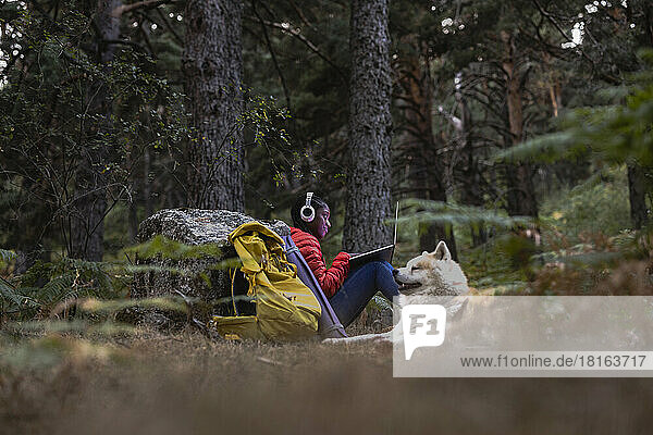 Woman wearing wireless headphones using laptop in forest