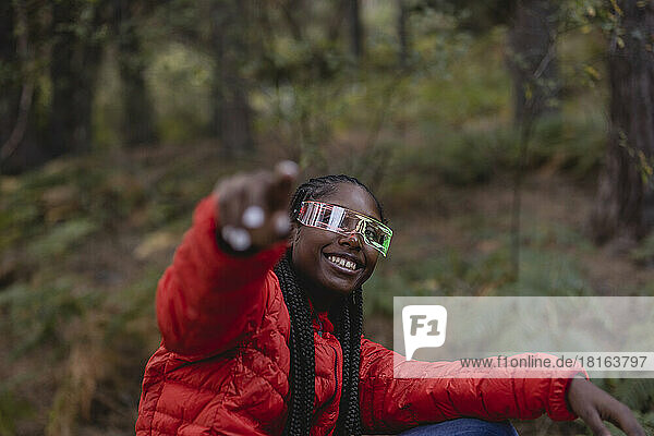 Happy woman wearing futuristic glasses gesturing in forest