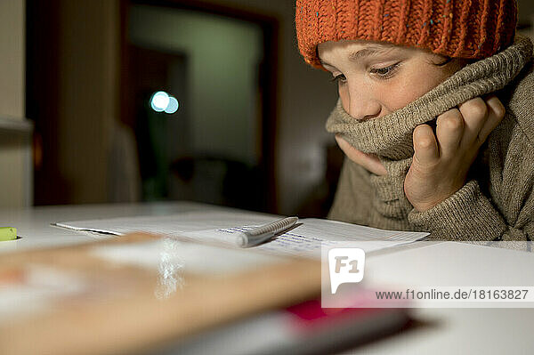 Junge in warmer Kleidung macht Hausaufgaben am Tisch