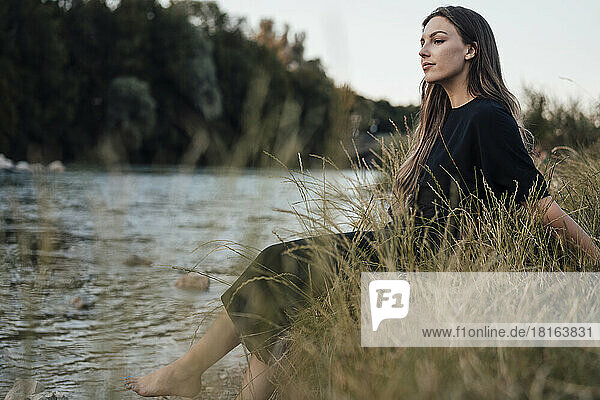 Thoughtful young woman with long hair sitting by lake