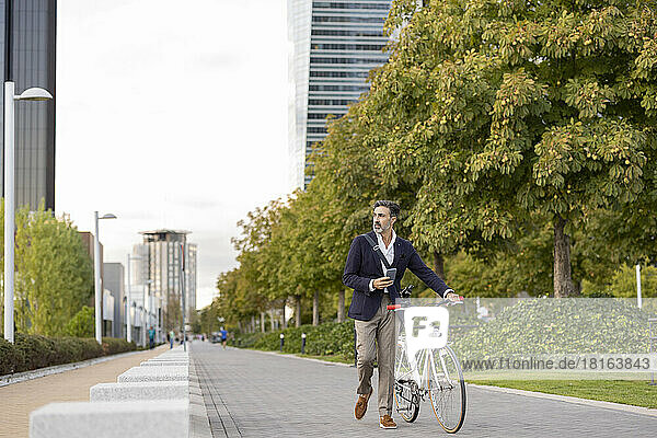 Businessman wheeling with bicycle on footpath