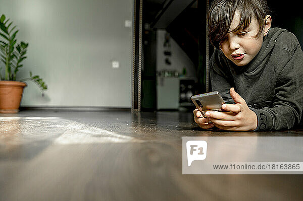 Boy using phone and lying on floor at home