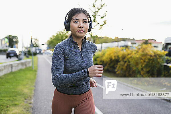 Young woman listening to music and jogging on road