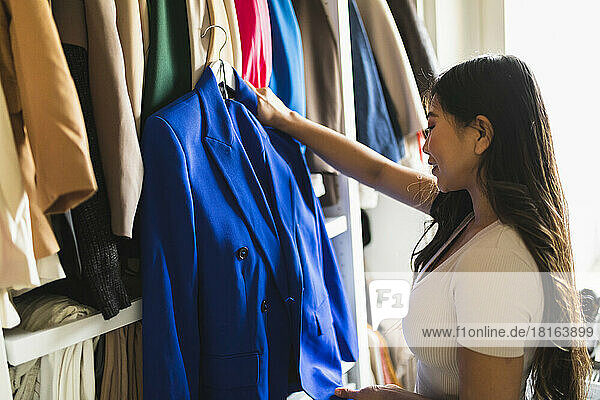 Smiling woman holding blue blazer standing in closet