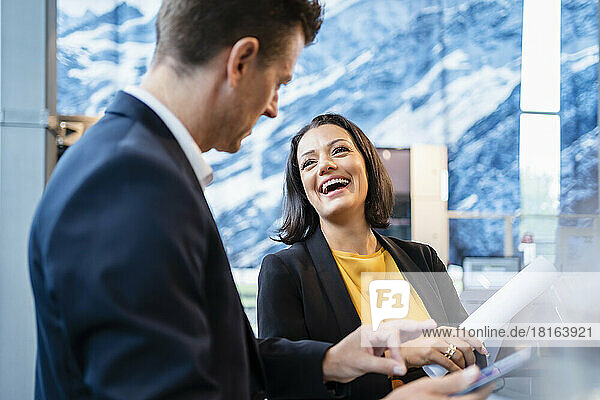 Happy businesswoman talking with businessman holding tablet PC in office