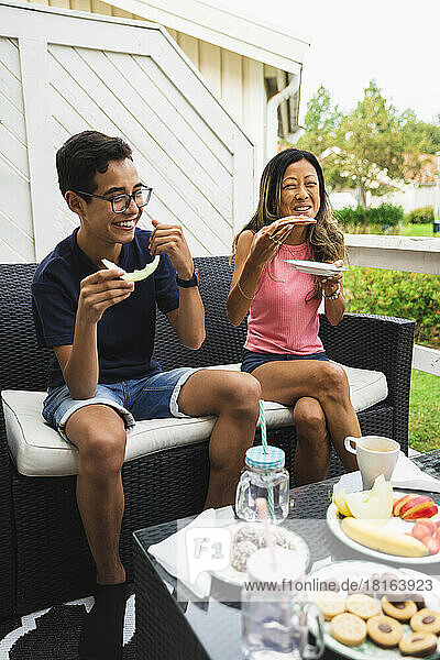 Happy woman enjoying snacks with son on couch at porch