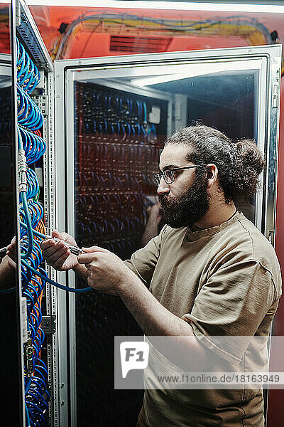 IT technician with beard connecting cables in server room