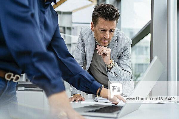 Businesswoman pointing at laptop and discussing with businessman at desk