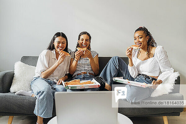 Happy roommates watching movie and eating pizza on sofa at home