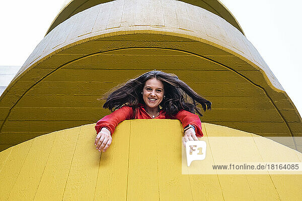 Glückliche junge Frau schaut aus gelbem Gebäude