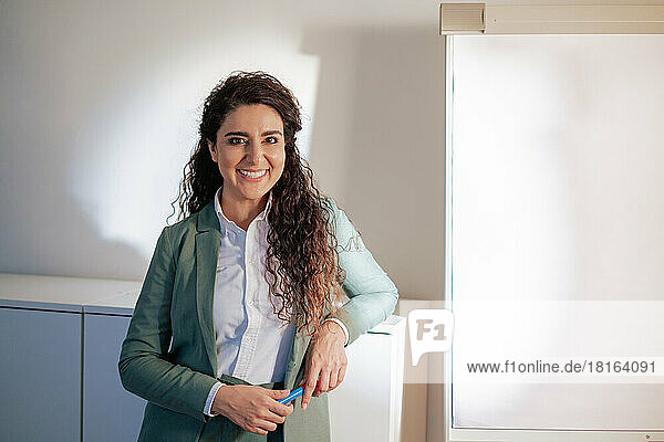 Smiling businesswoman leaning on cabinet at work place