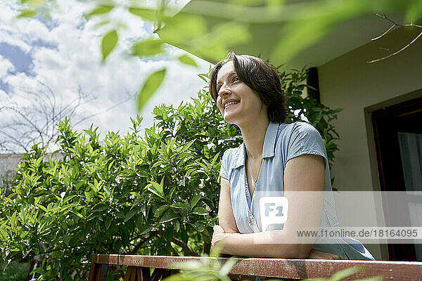 Smiling woman standing on balcony on sunny day