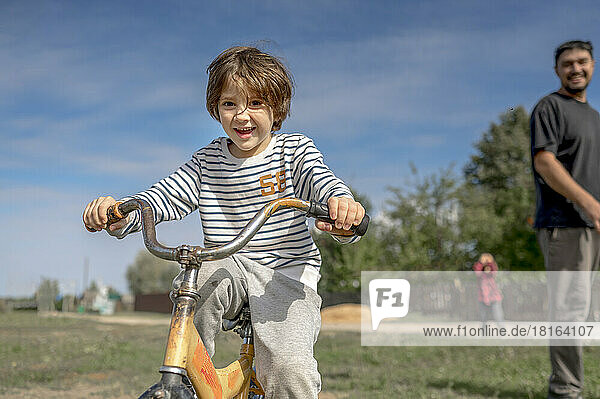 Lächelnder Junge  der an einem sonnigen Tag mit seinem Vater Fahrrad fährt