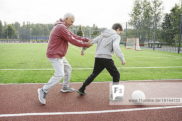 Happy grandfather with boy playing soccer at sports field