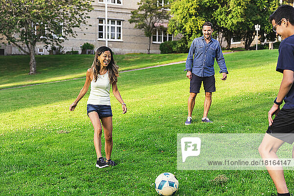 Glückliche Familie  die Fußball auf Gras im Rasen spielt
