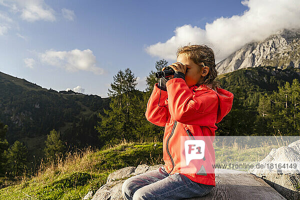 Girl looking through binoculars sitting on rock