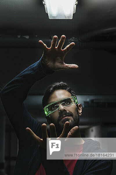 Man wearing futuristic smart glasses gesturing under illuminated light