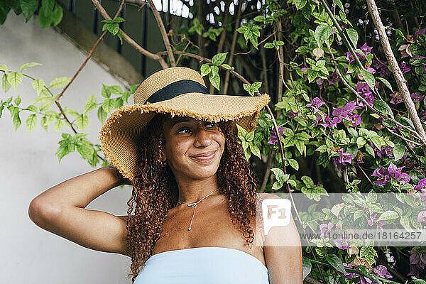 Lächelnde Frau mit Hut steht vor der Pflanze