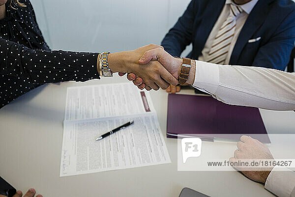 Geschäftsfrau schüttelt einem Kollegen am Schreibtisch im Büro die Hand