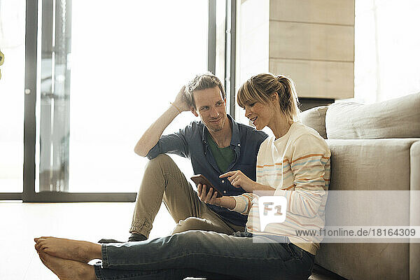 Pregnant woman holding smart phone talking with man sitting at home