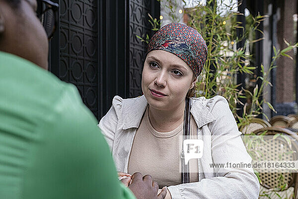 Woman wearing bandana talking with friend at sidewalk cafe