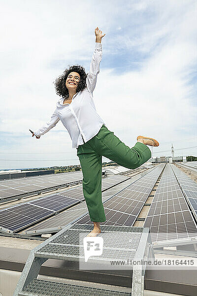 Happy businesswoman with hand raised in front of solar panels on rooftop