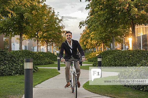 Fröhlicher Pendler fährt Fahrrad auf Fußweg im Park