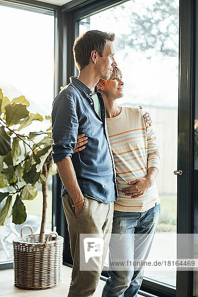 Expectant couple with arm around each other standing at home